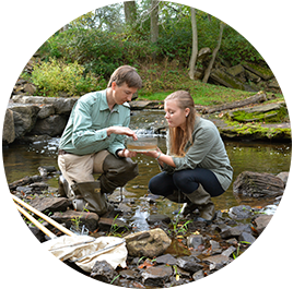 Professor and student kneeling near stream