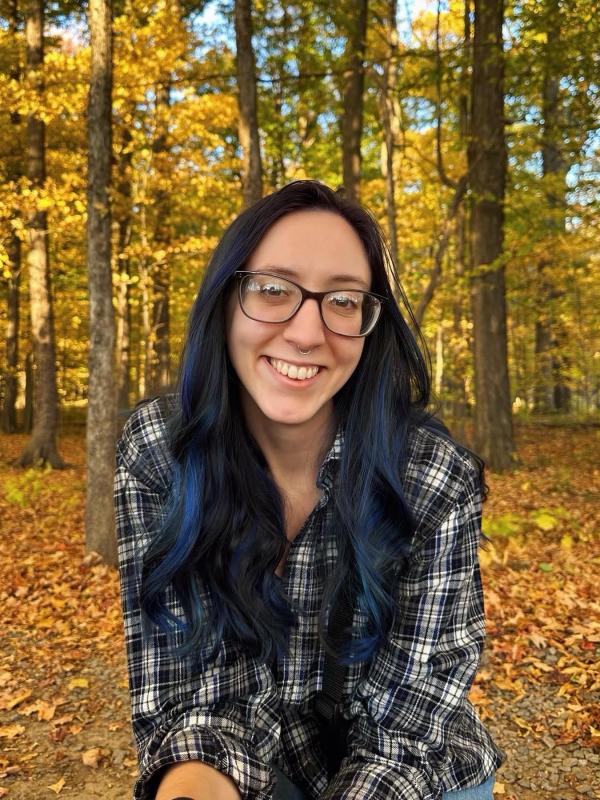 Courtney Gazda Courtney smiling on a sunny day surrounded by foliage.