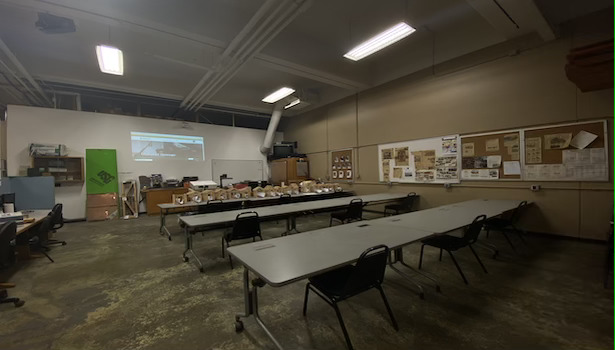 This photo shows the classroom from the back. Showing student chairs, projector and professor podium.