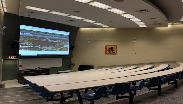 Photo of the back of the classroom. Including chairs and the projection screen. 