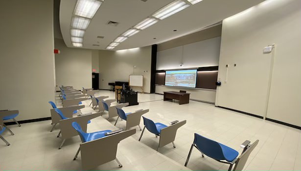 Photo of the classroom from the back left of the classroom. Showing the projector screen and student chairs. 