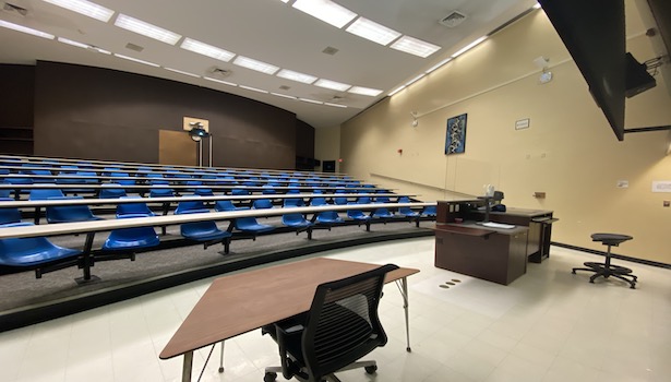 Photo shows the classroom from the left side of the room including the podium and student chairs. 