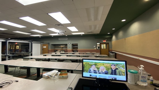 Photo shows the front of the classroom including projector screen, podium, and student seats. 