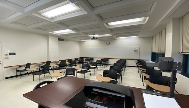 Photo shows the back of the room from the podium perspective. Including student seating and the front of the podium. 