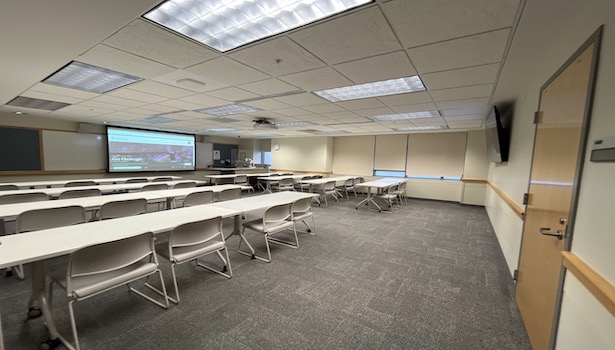 photo shows the front of the room from the back left including podium and student chairs. 