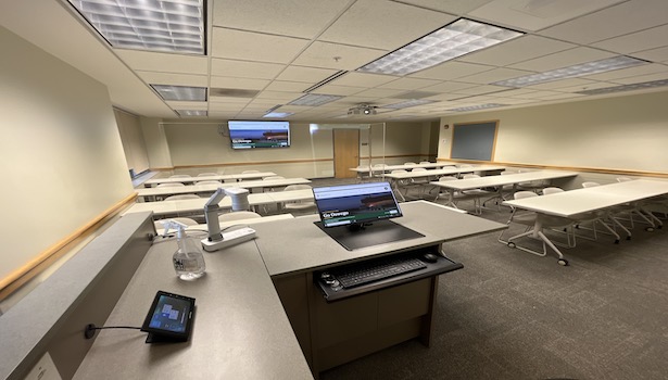 photo of the classroom from the podium perspective. Including student chairs and professor monitor/confidence monitor in the back of the room.  