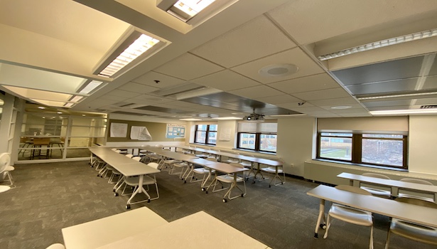 Photo shows the classroom from the podium perspective left side including student chairs and the projector. 