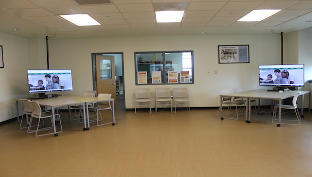 Photo of the back of the classroom from the center of the room. Including 2 student workstations and chairs. 