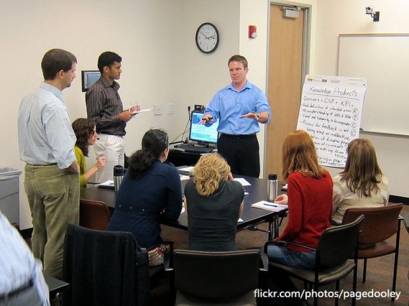 People sitting and standing around an instructor teaching a course