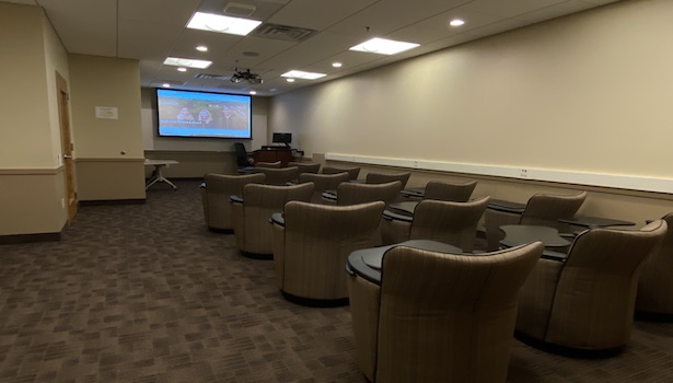 Photo of the front of the classroom from the left side of the room. Showing student chairs and projector screen. 