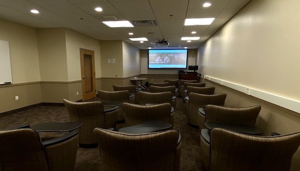 Photo of the front of the classroom from the center. Showing student chairs and projector screen