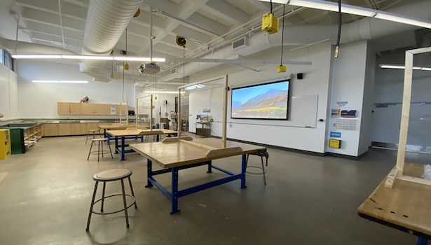 Photo shows the front of the classroom from the back right side. Including professor cart MAC and projector screen.