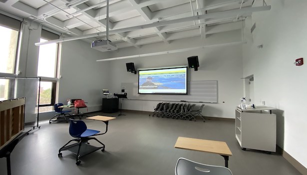 Photo of the front of the classroom showing a student chair, and the projector screen