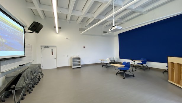 Photo showing the back of the classroom from the podium perspective. Including the piano and a few chairs