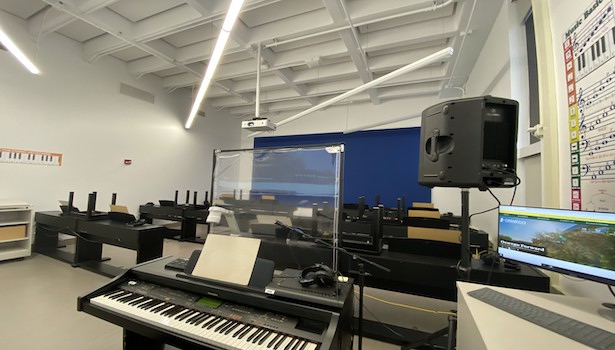 Photo showing the back of the classroom from the podium perspective. Showing professor piano, student pianos and part of the podium computer. 