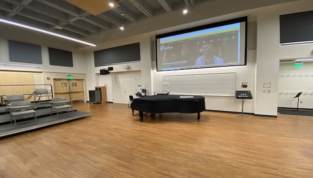 Photo shows the back of the classroom with the "podium PC" and projector screen. 