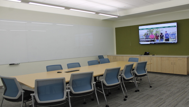 Photo of the classroom from the back of the room showing the conference table and flatscreen display