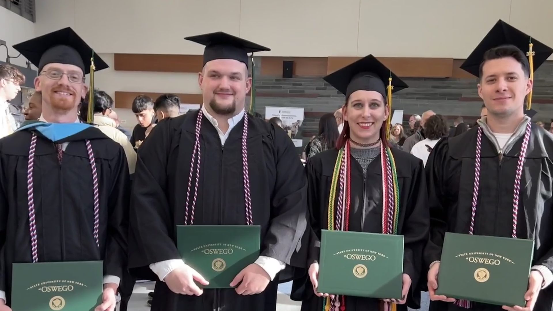 Four graduates dressed in commencing regalia, holding their diplomas