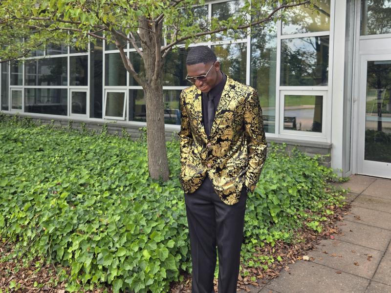 Oswego student Jamal Akin-Tukur stands outside Marano Campus Center wearing a gold blazer and black dress pants.