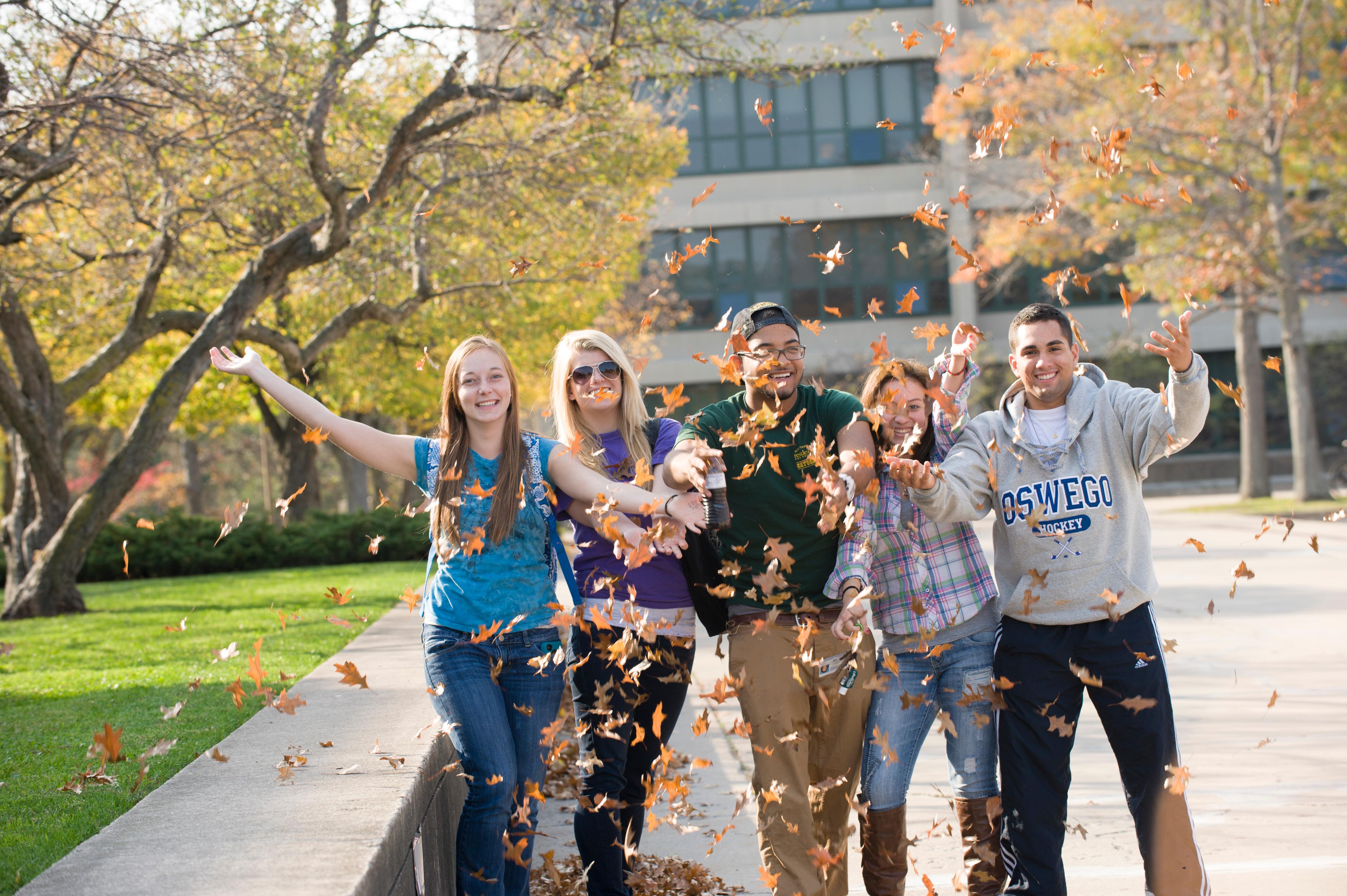 SUNY Oswego students toss leaves in the air to celebrate the fall season.