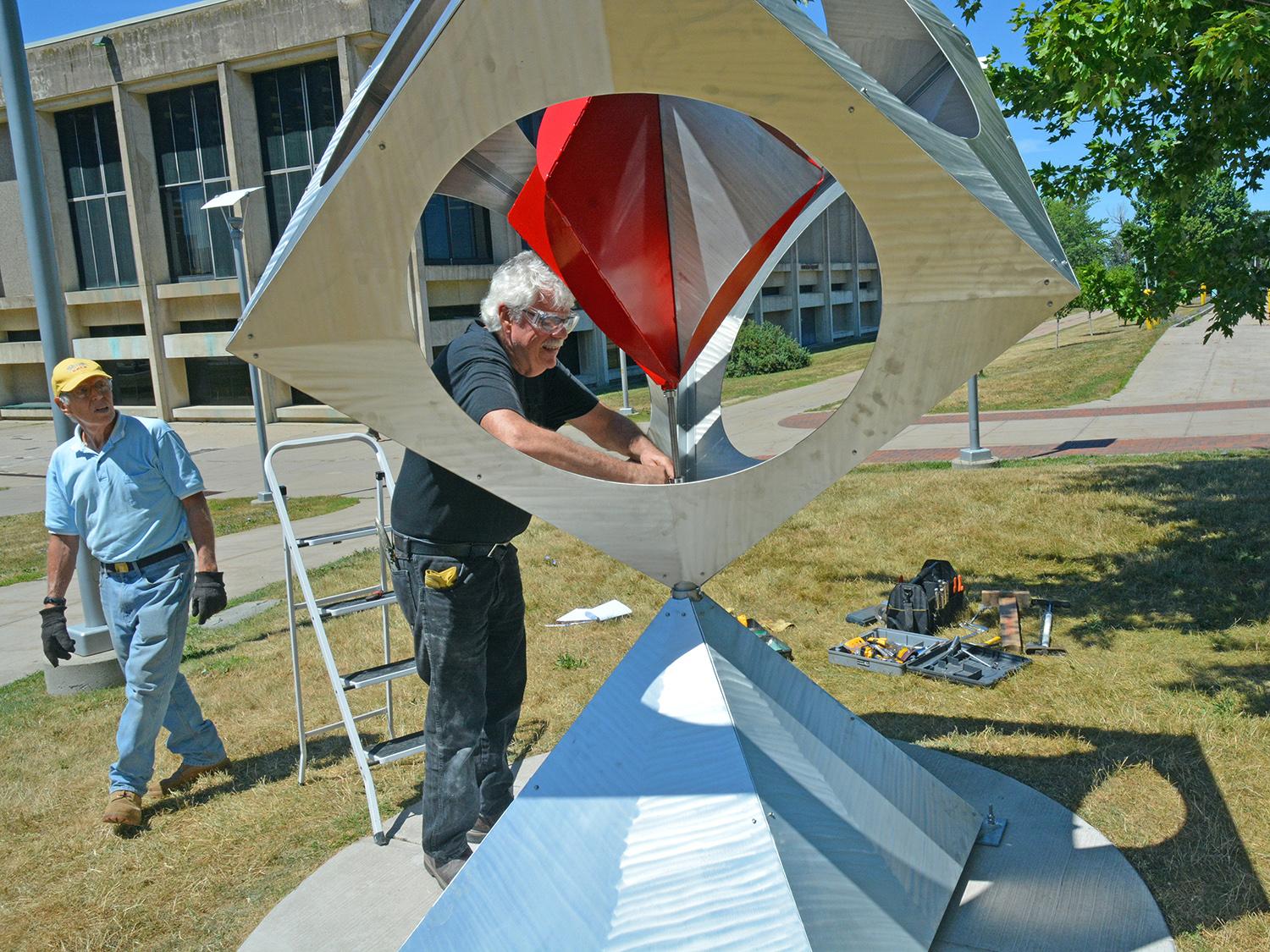 Artist Bob Turan with his sculpture that features a pinwheel in a box upon a pyramid