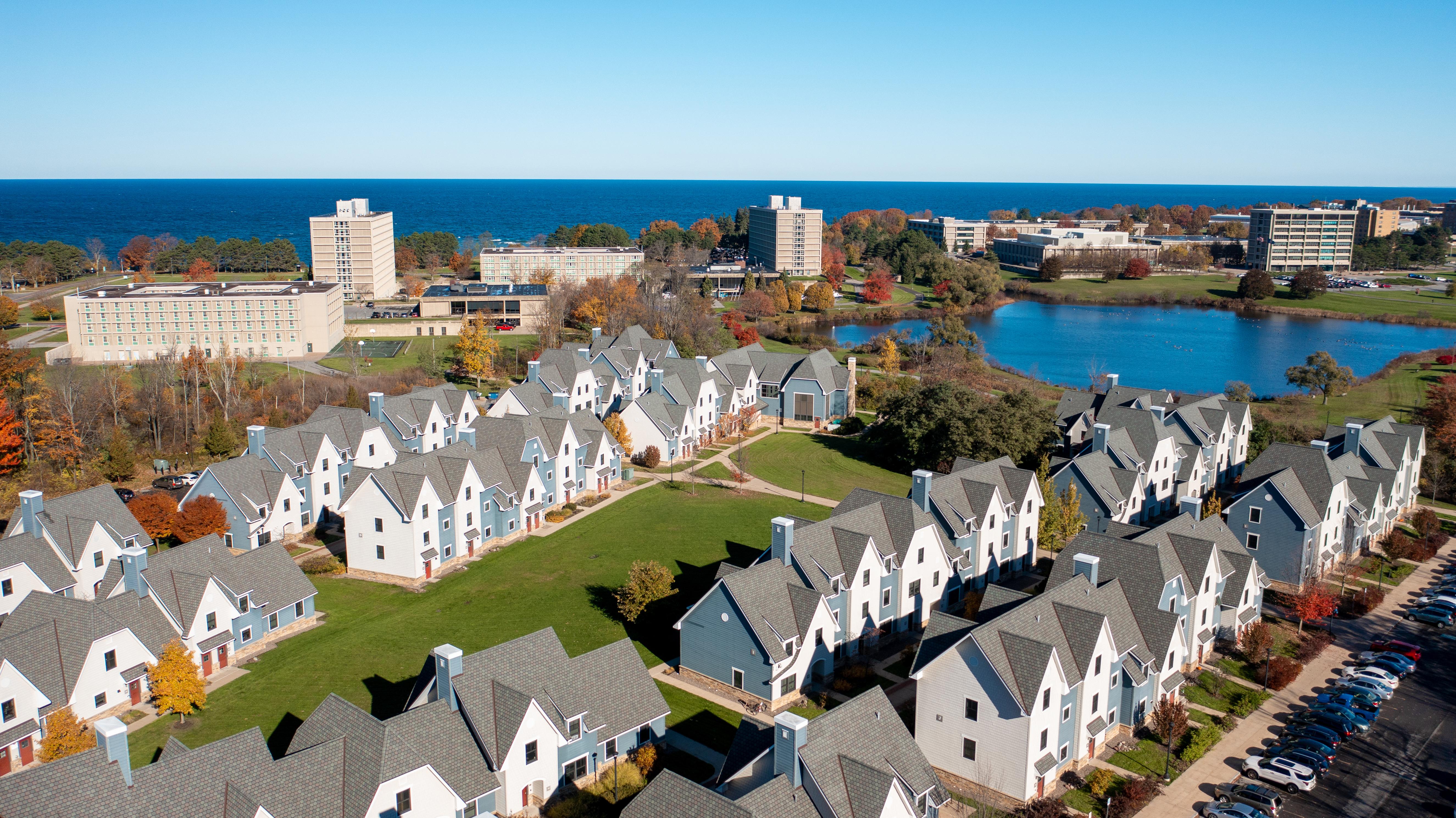 Aerial view of campus with The Village in the foreground, Glimmerglass Lagoon and a background of lakeside buildings and Lake Ontario