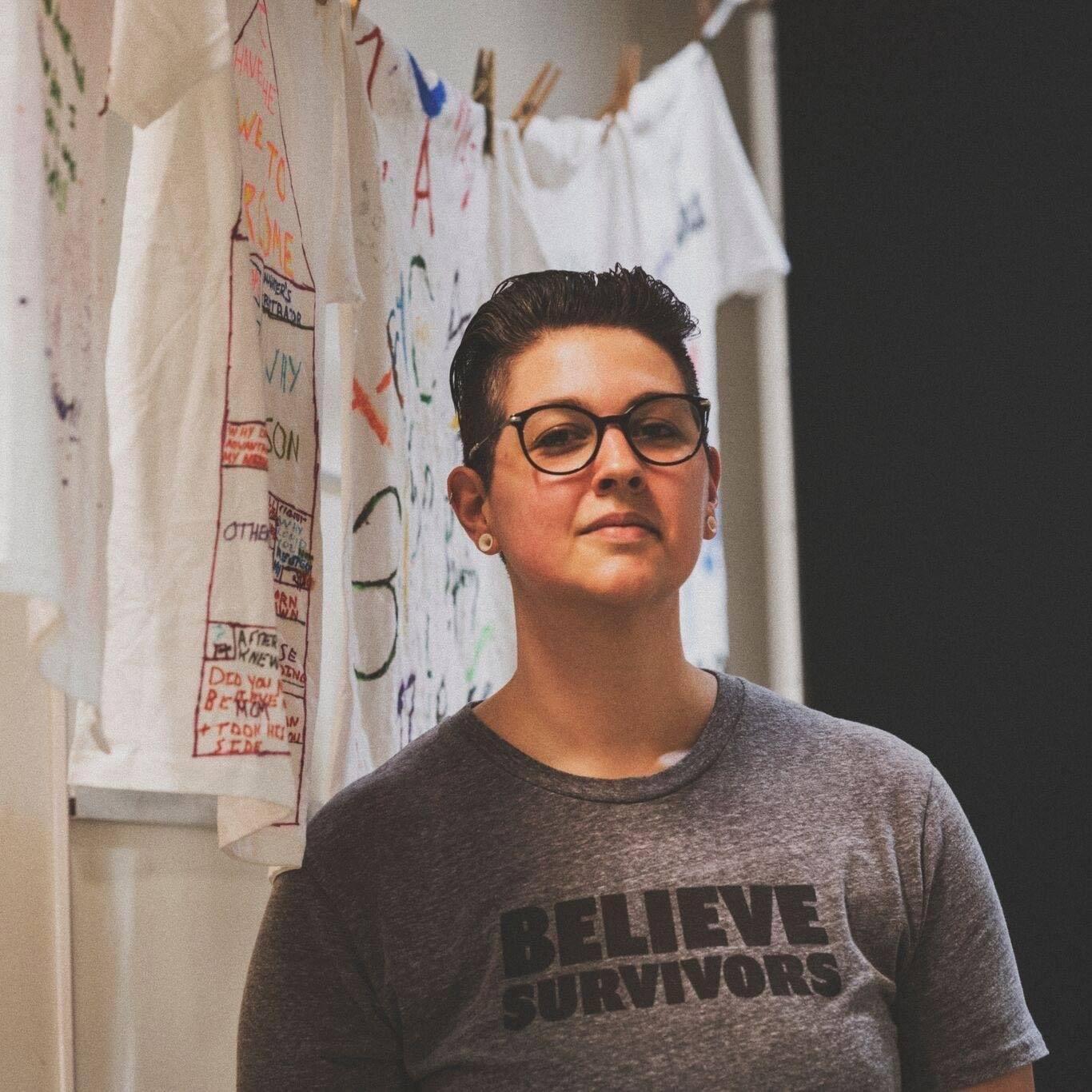 Alex Dukat next to an awareness clothesline project and a T-shirt reading Believe Survivors