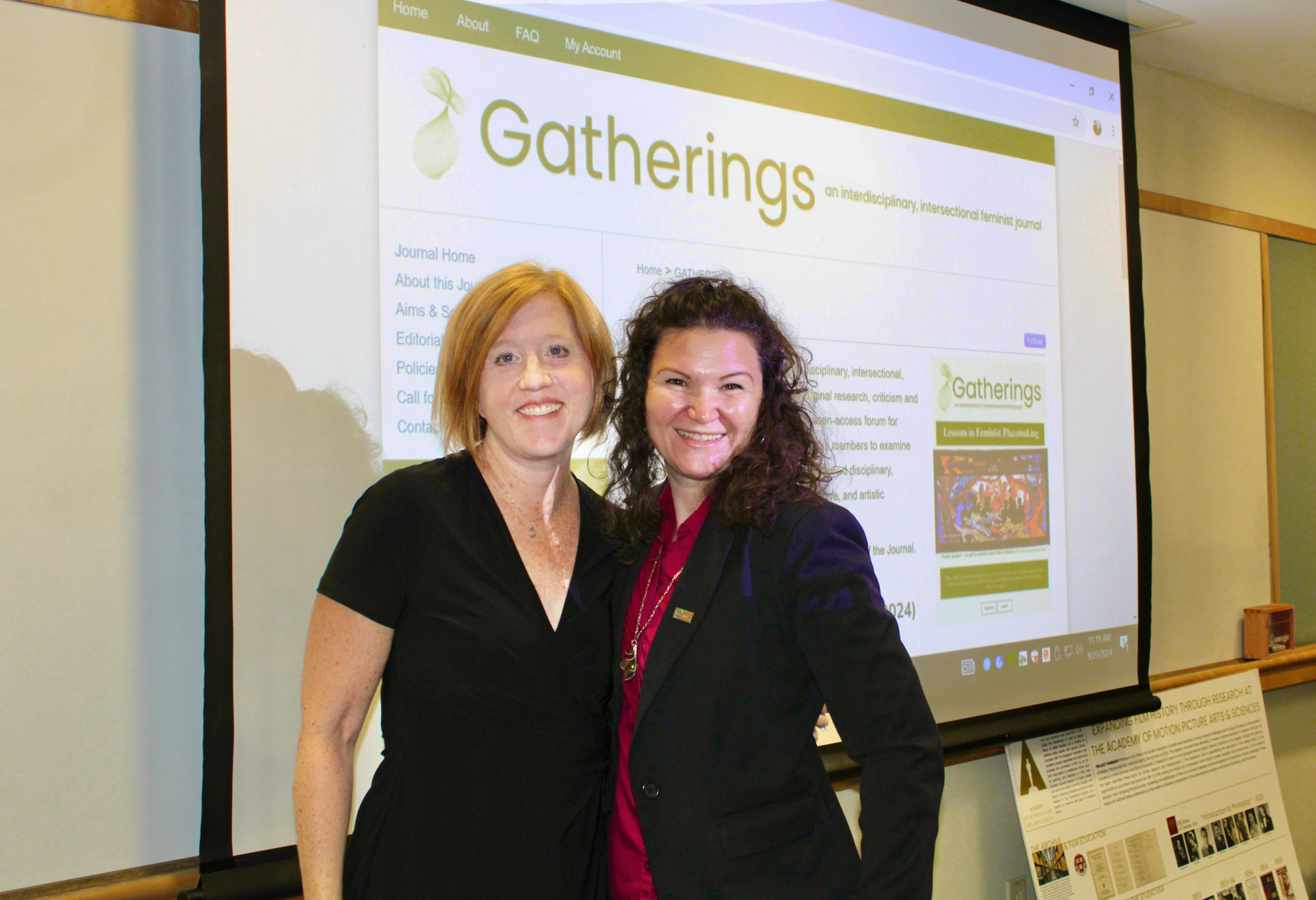 Cinema and Screen Studies professor Dr. Amy shore and English and Latin American studies studies professor Dr. Roberta Hurtado stand in front of the website for "Gatherings: An interdisciplinary and intersectional feminist journal."
