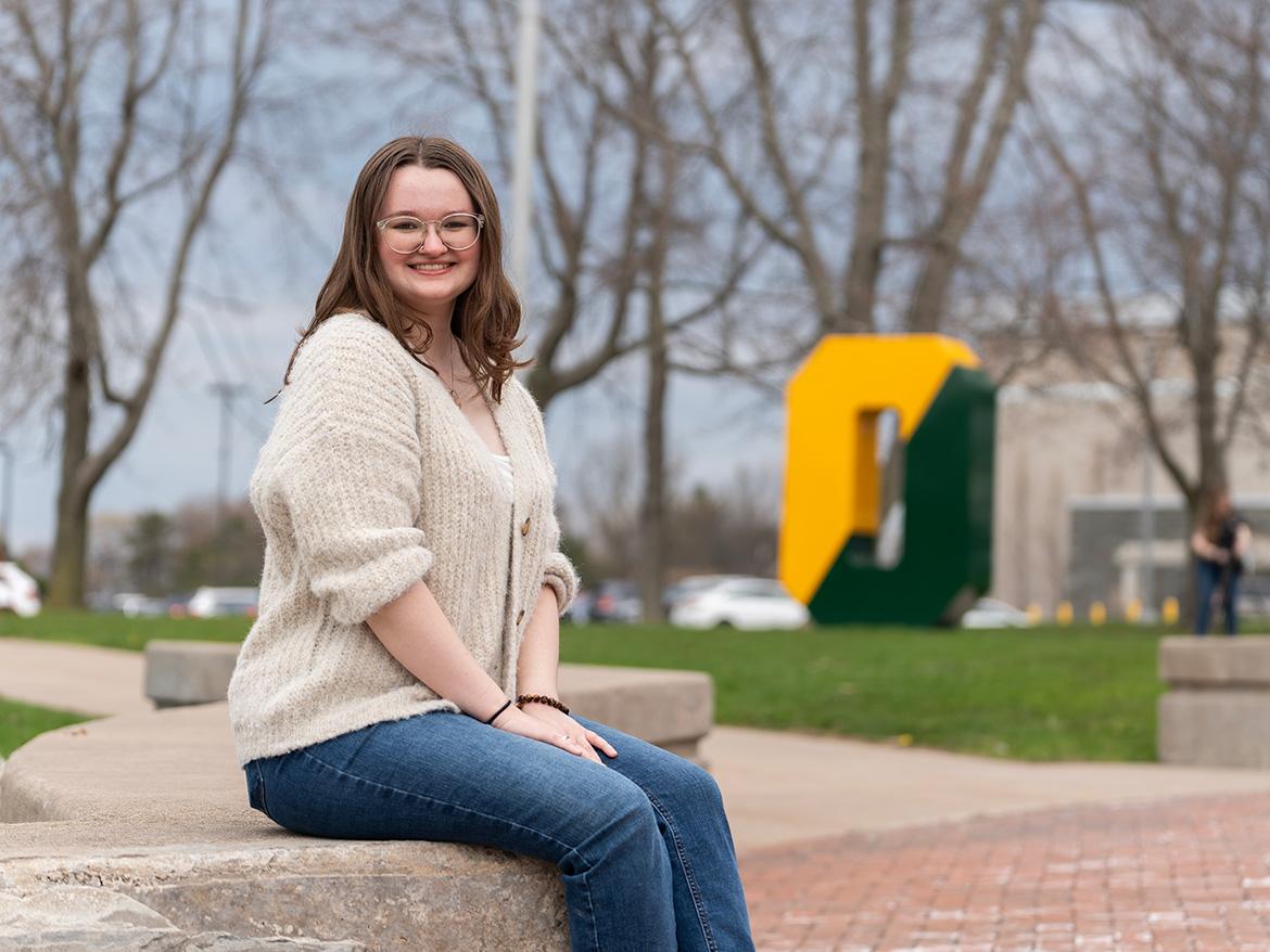 student posing by the spirit o on the quad
