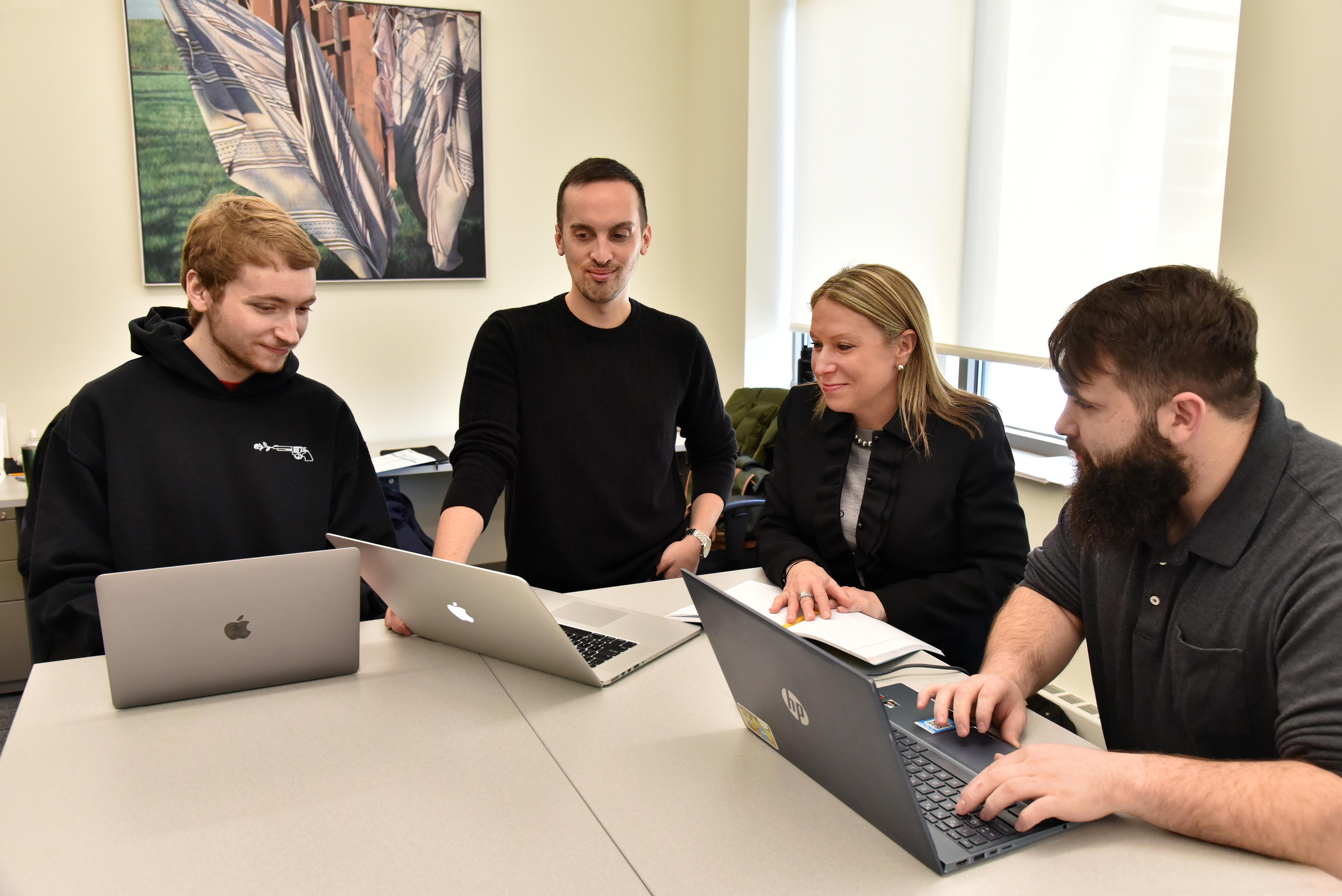 Three school psychology master's students and a faculty member look over some work on laptops