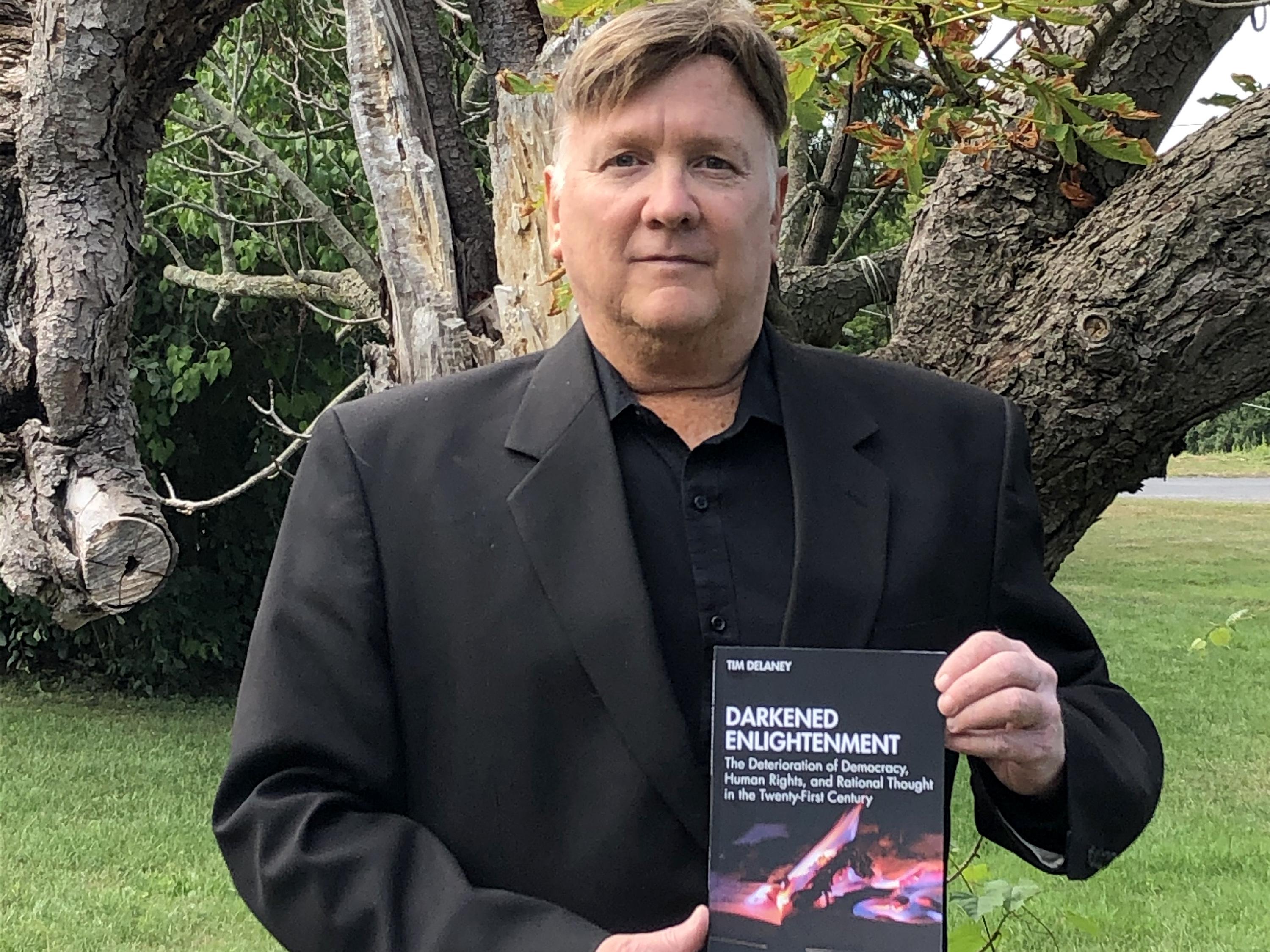 Tim Delaney holding new book, Darkened Enlightenment