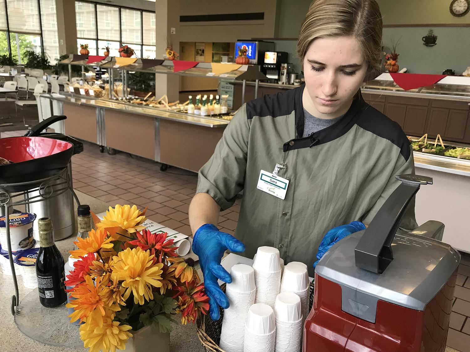 Sara Meal refills paper condiment cups in a dining hall