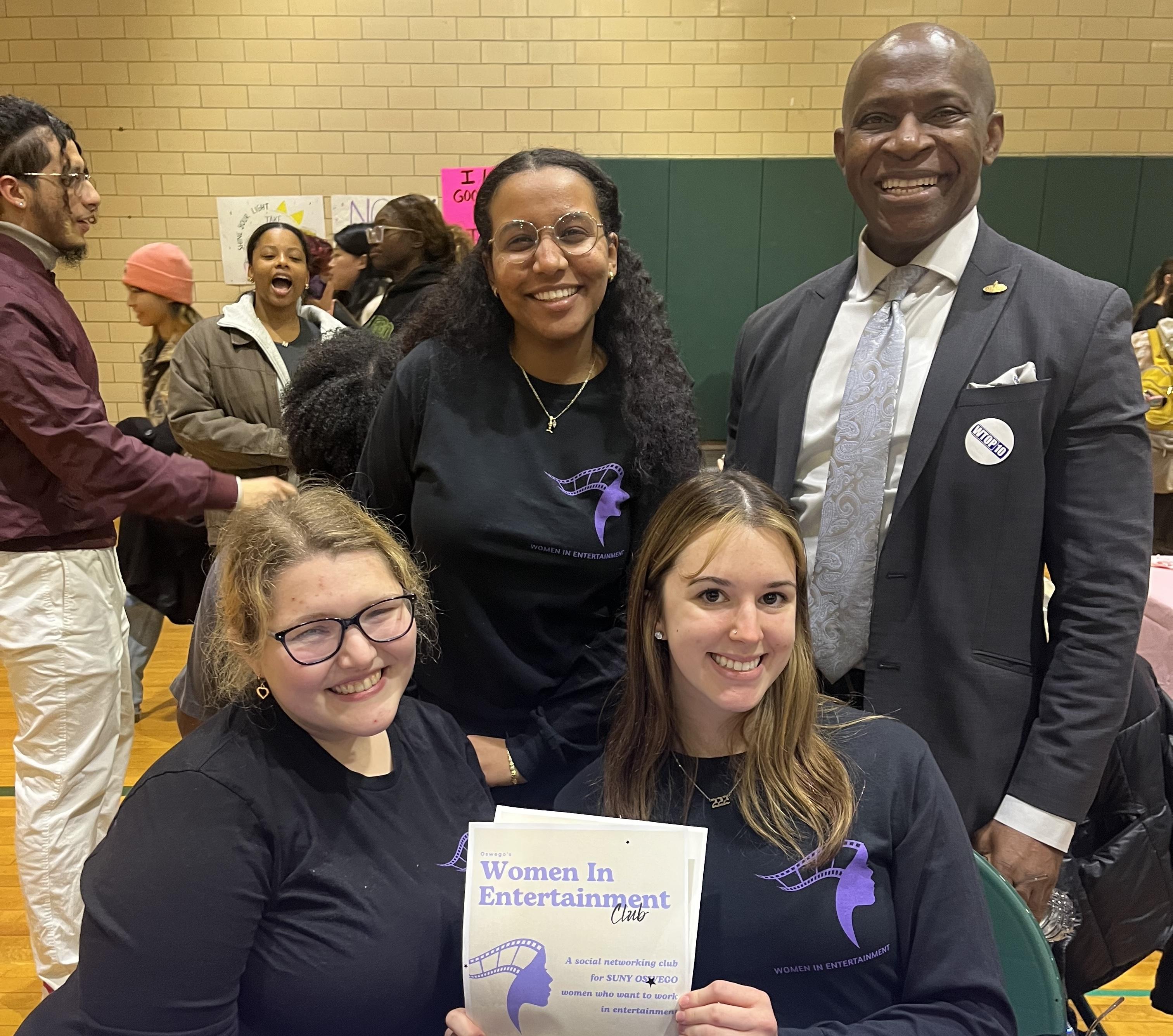 Student executive board members of the Women In Entertainment Club pose for a photo with President Nwosu at their Student Involvement Fair table.