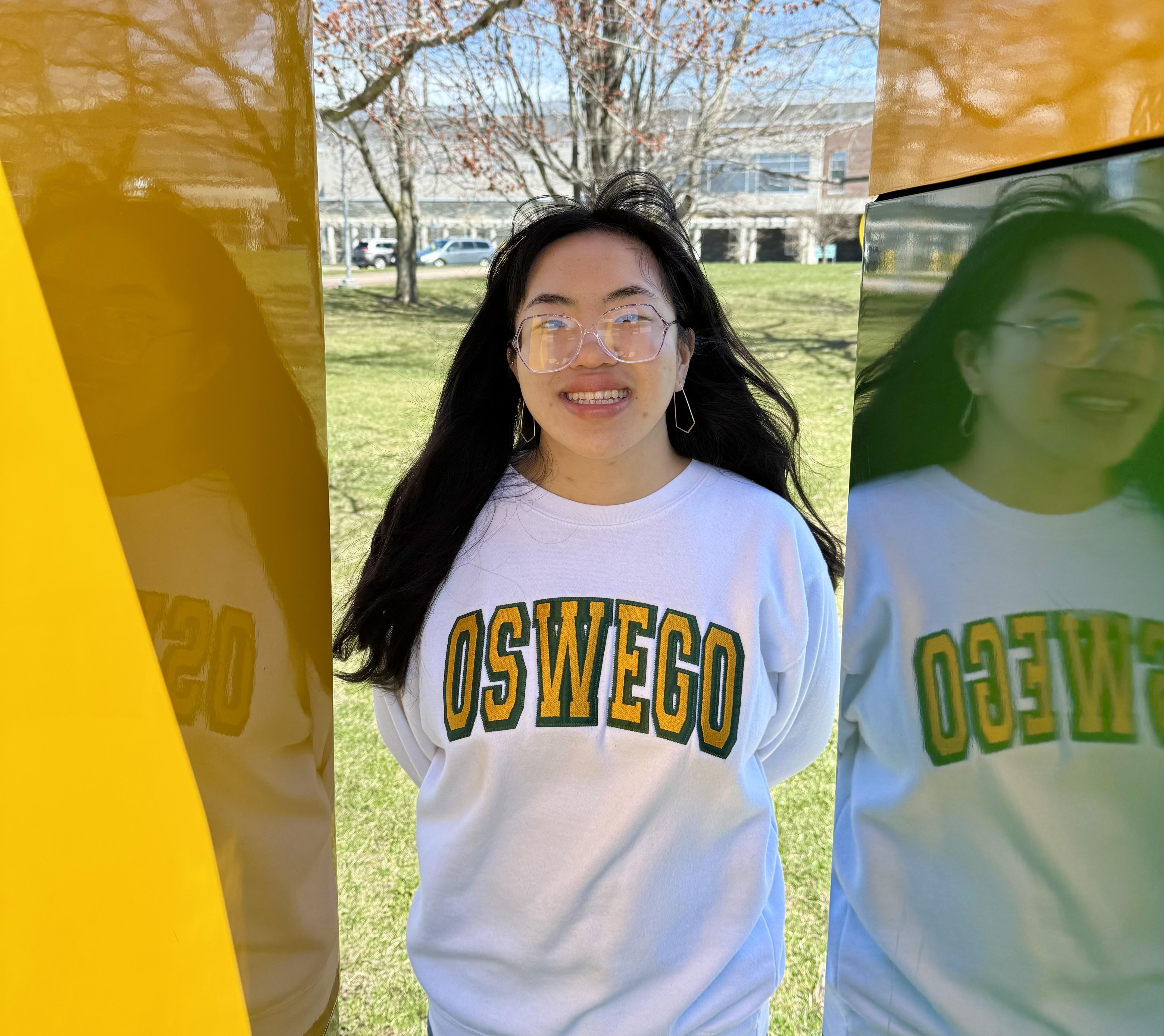 SUNY Oswego student Emma Halsey stands inside the green and gold "O" statue on SUNY Oswego's campus.