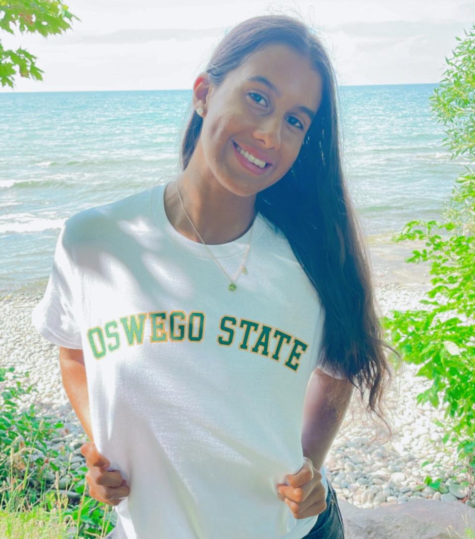 Jolie Santiago poses by Lake Ontario in a white Oswego State T-shirt