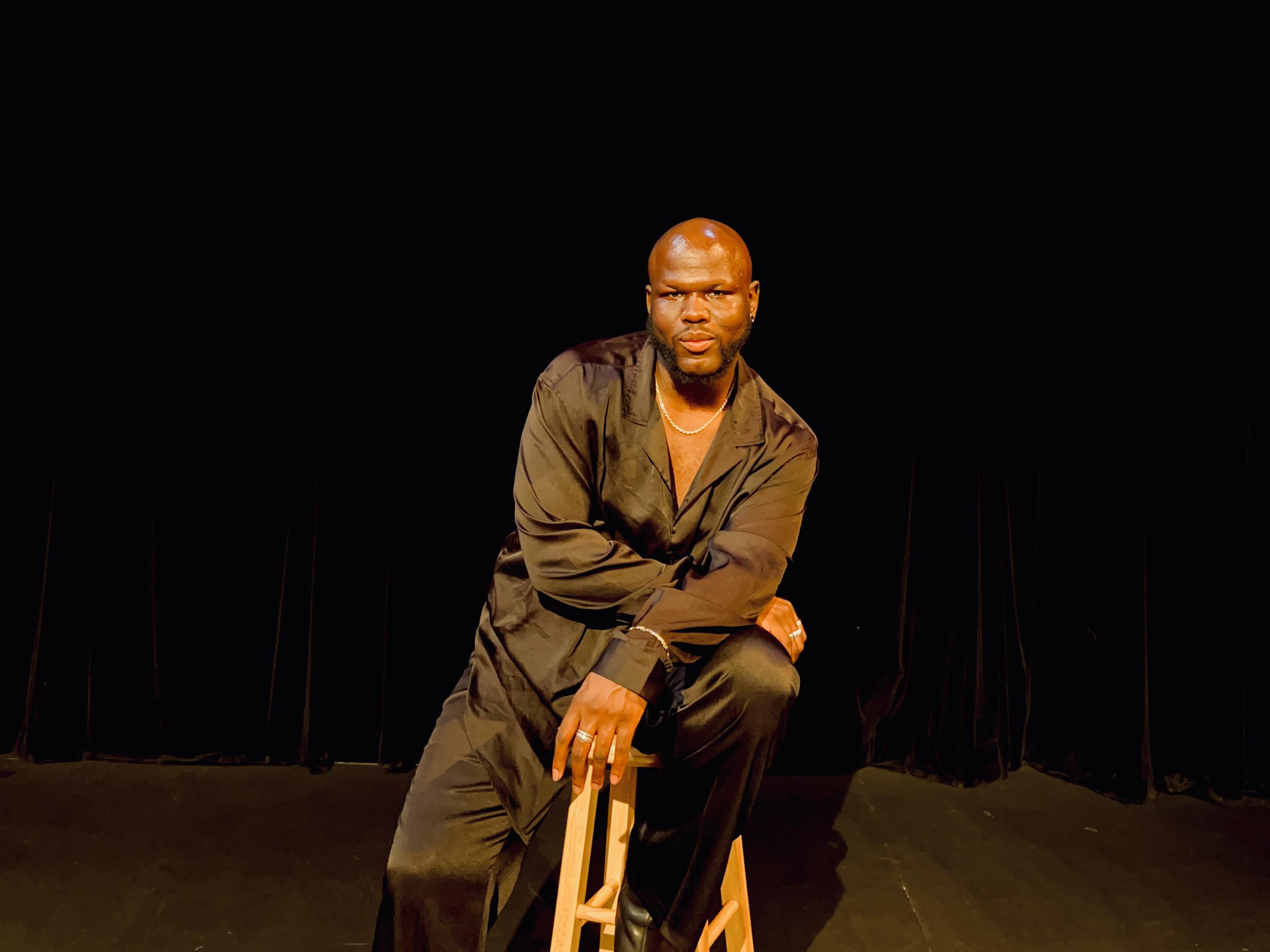 Lester Mayers pictured on an unadorned stage, a black curtain behind him