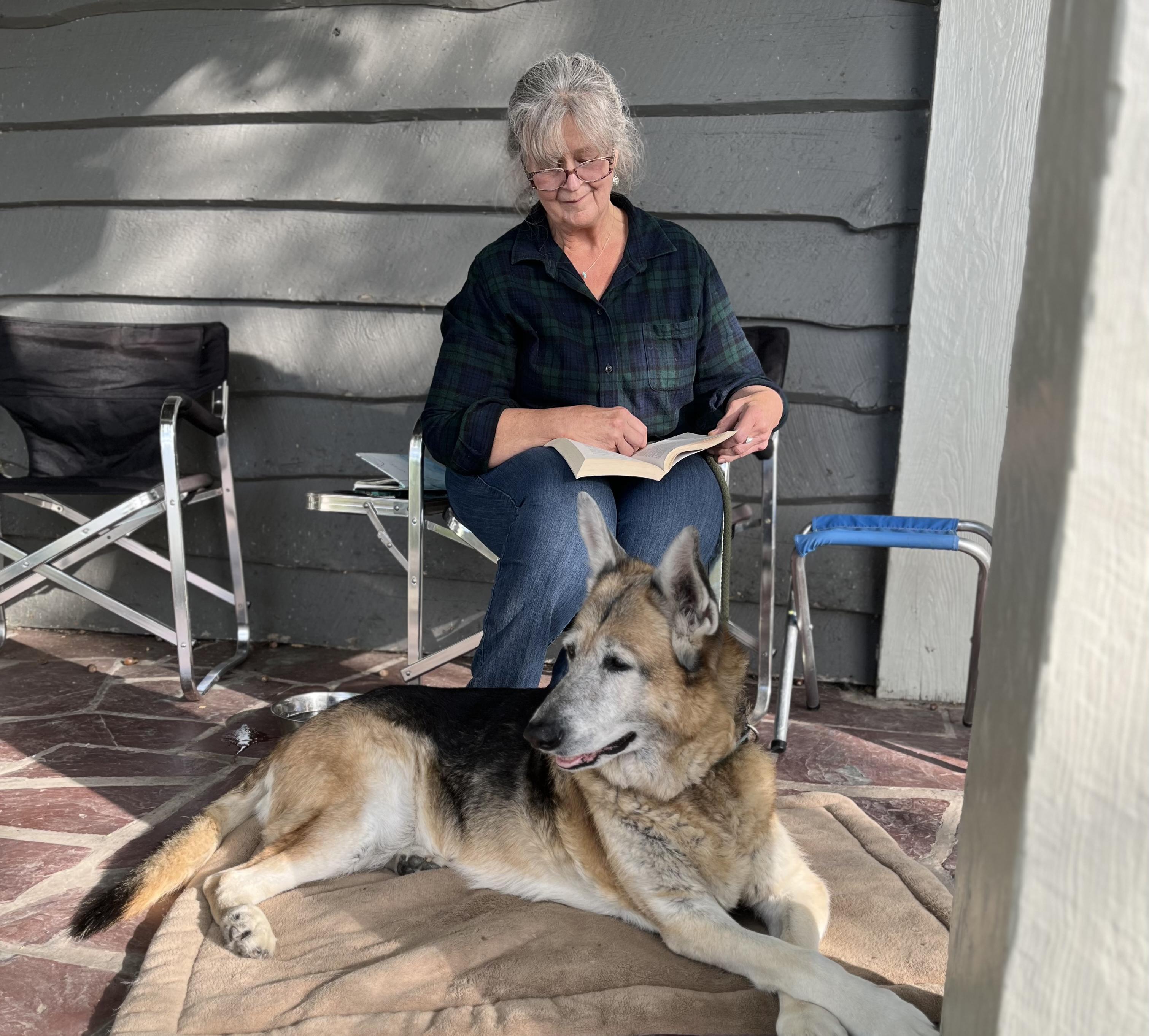 Linda Knowles reads on a porch with dog