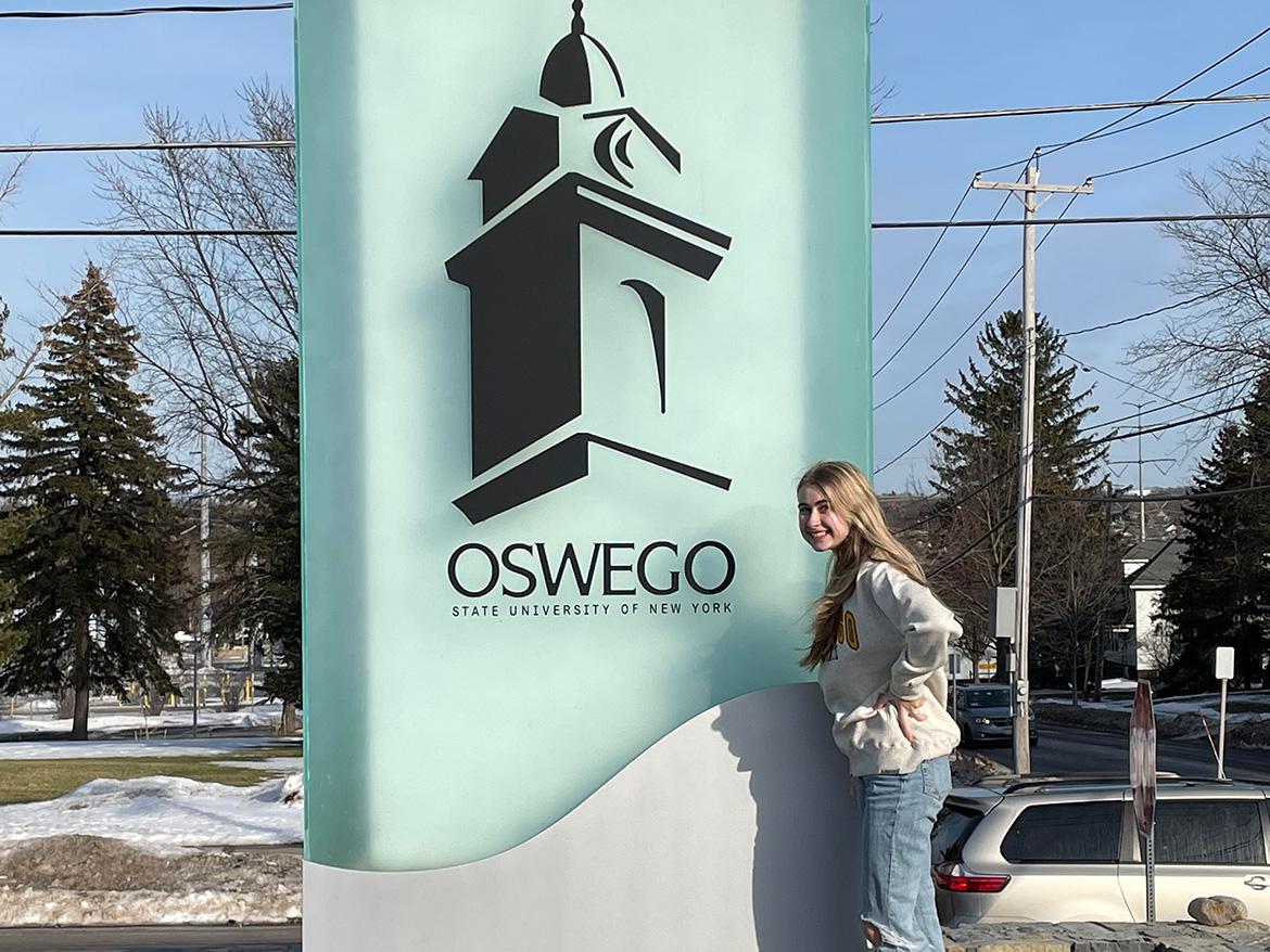 student standing by the suny oswego sign