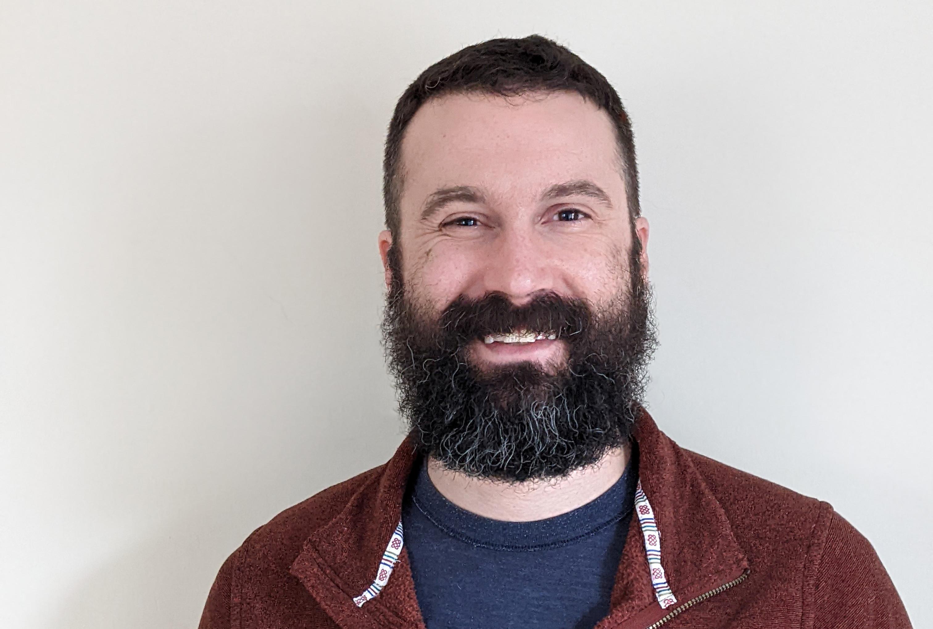 Headshot of Remmington Johnson wearing a maroon button up. Remmington has dark brown hair that is salt and pepper with a beard