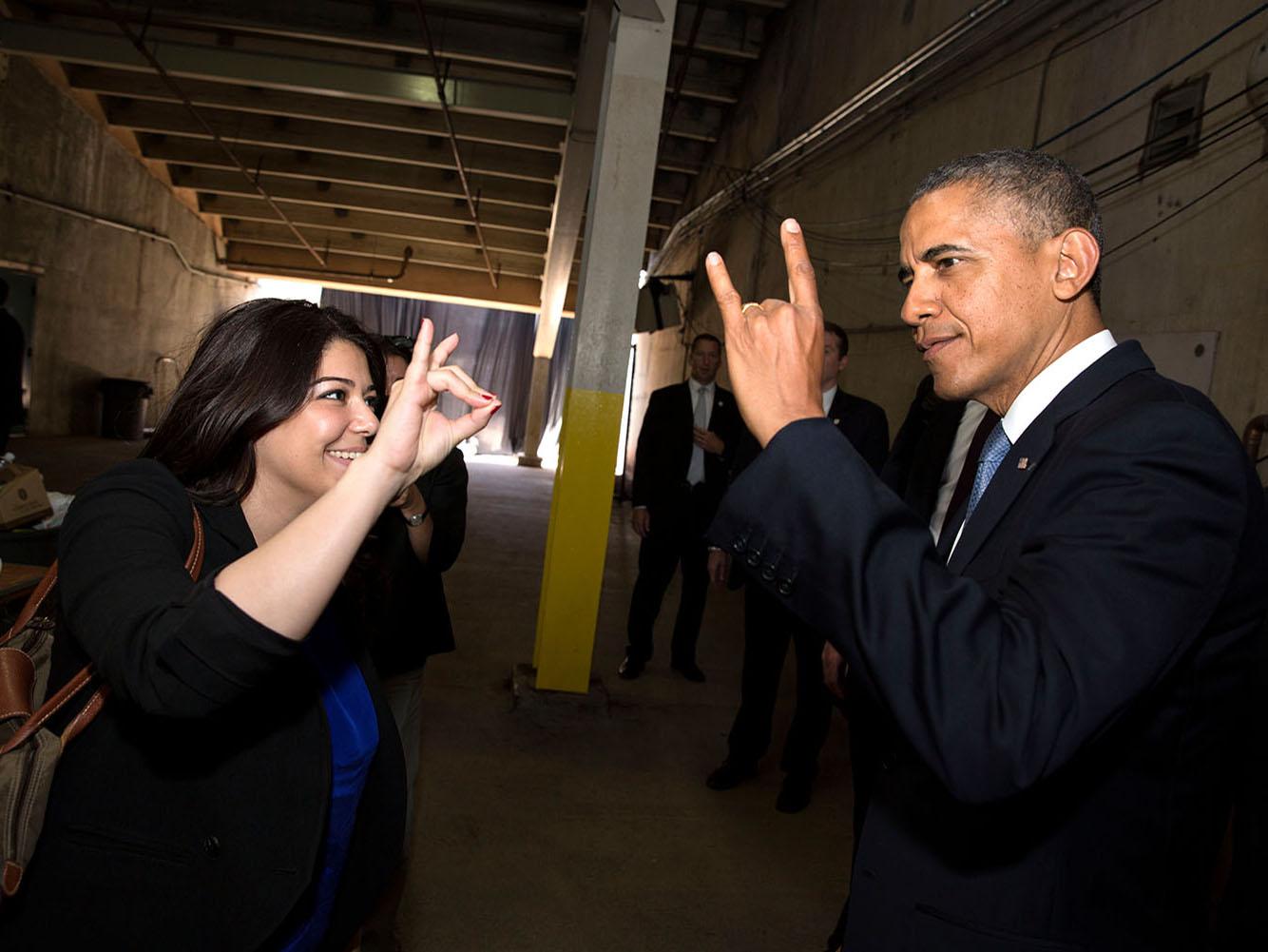 President Barack Obama's Personal Secretary Ferial Govashiri shows him how to make the sign of the anteater, mascot of the University of California, Irvine, prior to the UCI commencement at Angels Stadium in Anaheim, Calif., Saturday, June 14, 2014.