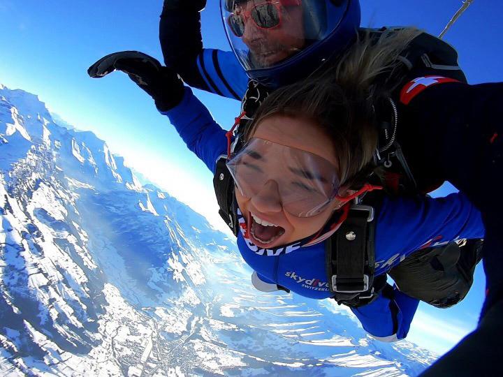 Student skydiving above the Alps, wearing look of exhilaration