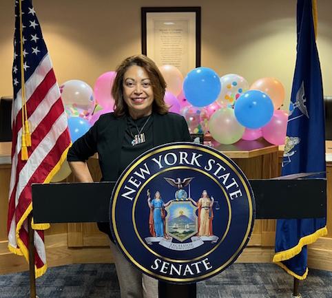 Maggie Rivera posing behind the senatorial seal during an awards ceremony