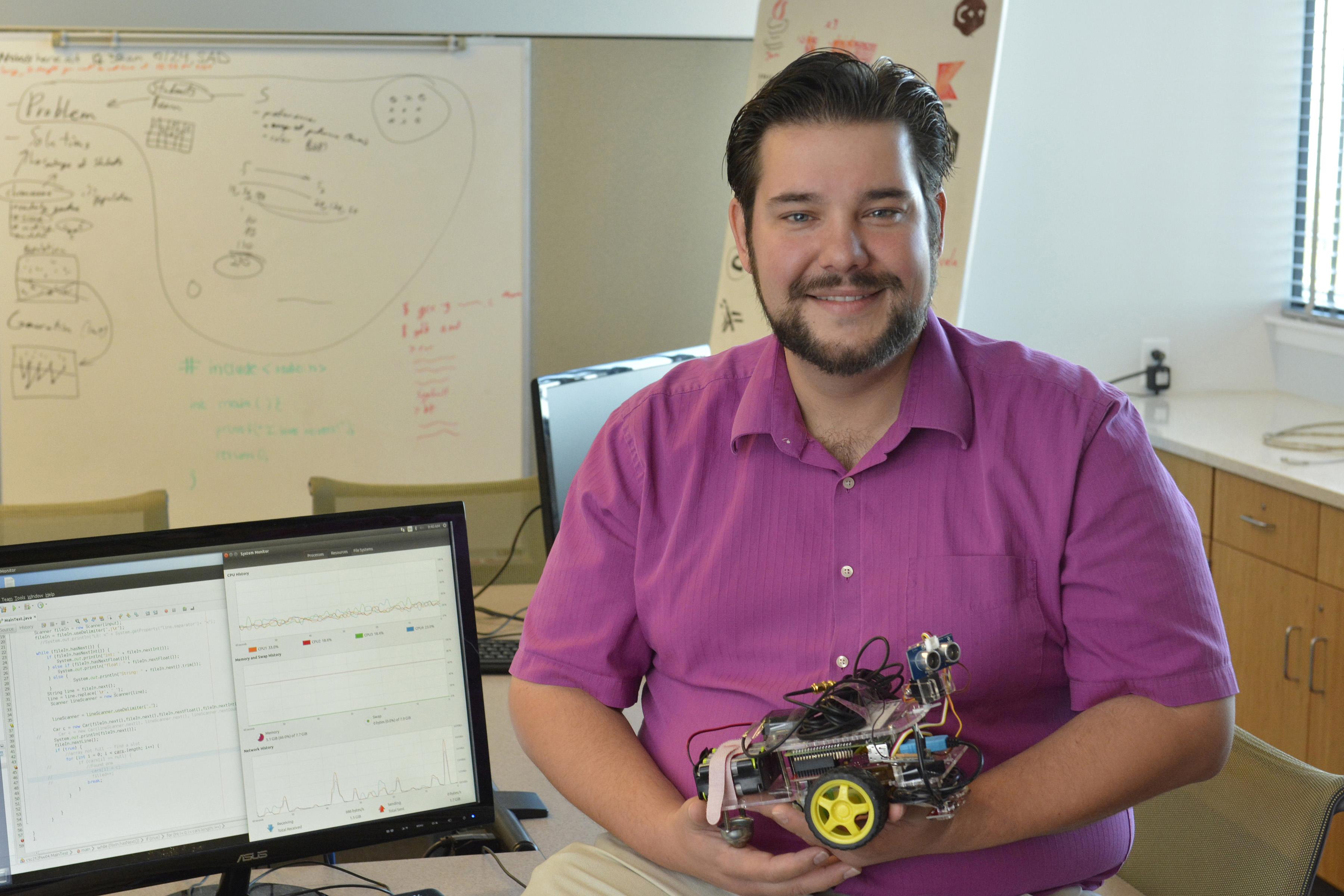 Computer science faculty member Bastian Tenbergen holds a small robotic car in his office