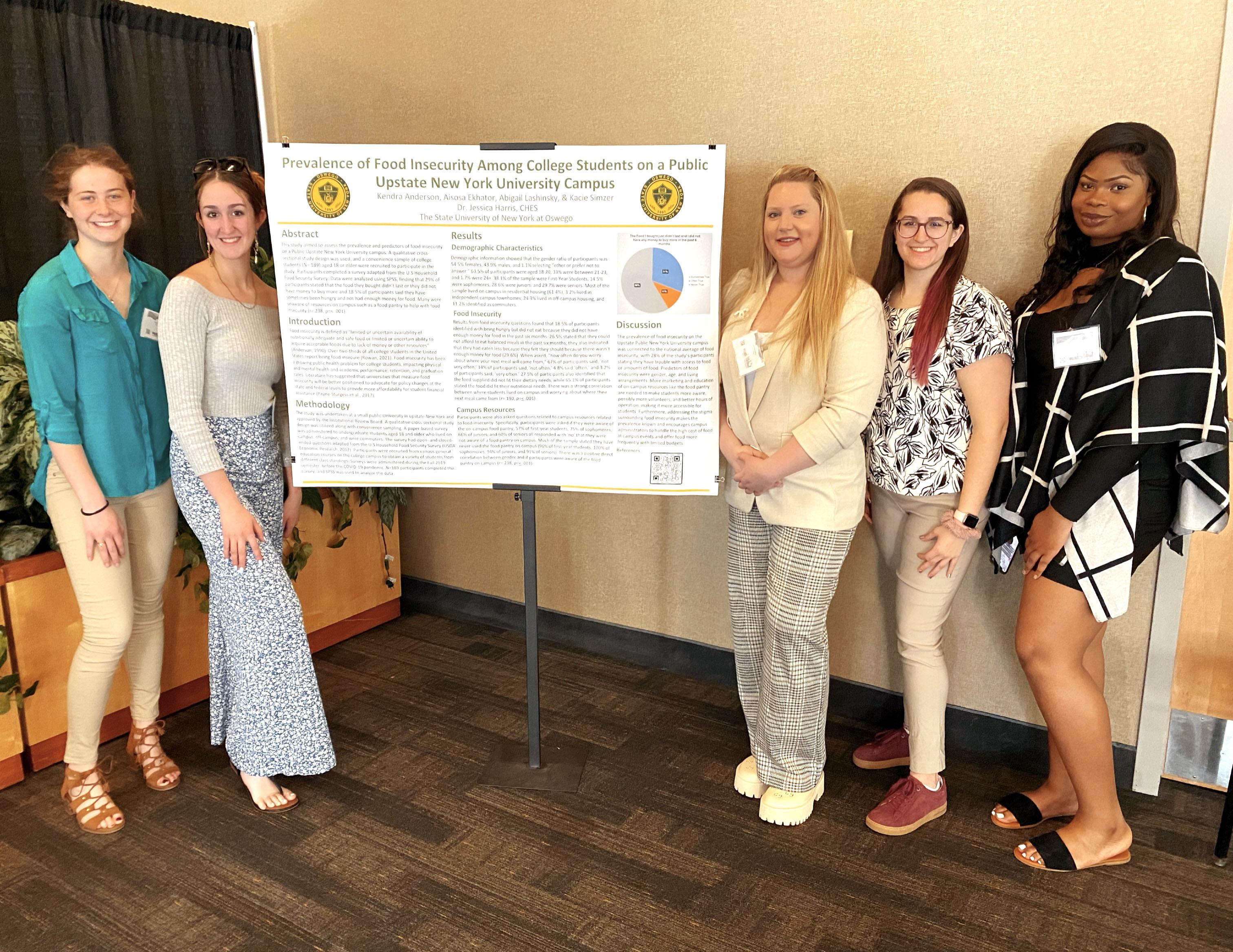 Faculty member Jessica Harris and four wellness management student pose with a poster they presented at a statewide conference