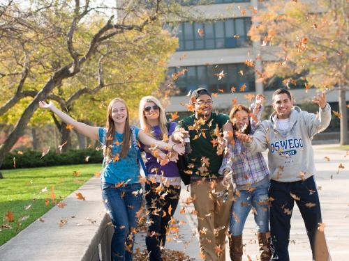 SUNY Oswego students toss leaves in the air to celebrate the fall season.