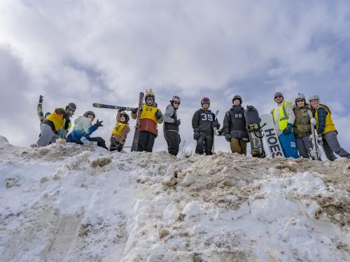 Skiers and snowboarders smile while standing atop a giant snow mound at a past Rail Jam