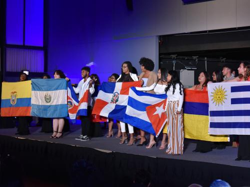 Students hold flags of many nations at 2018 ALANA Fashion Show