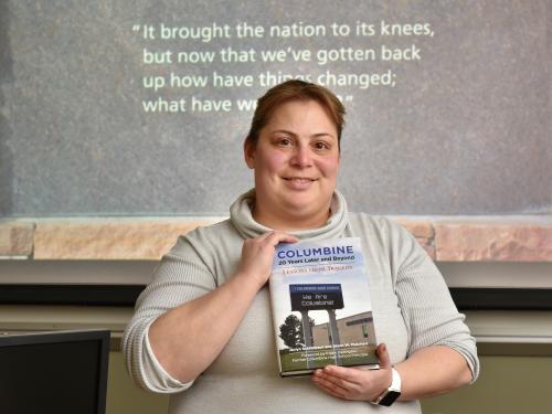 Jackie Schildkraut with book on 20th anniversary of Columbine, with quote from healing wall on screen behind her