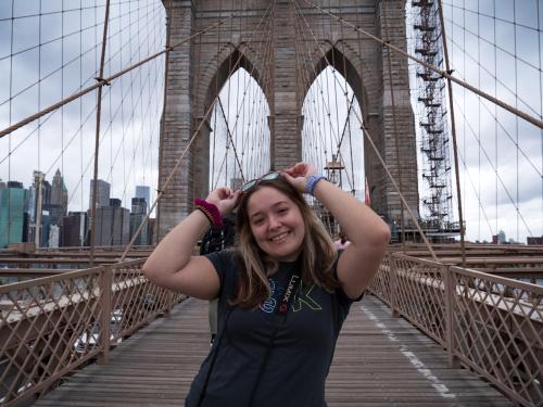 Alum Corey Cesare smiling with a camera on the Brooklyn Bridge.
