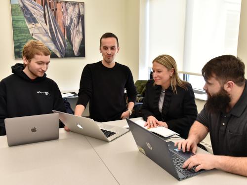 Three school psychology master's students and a faculty member look over some work on laptops